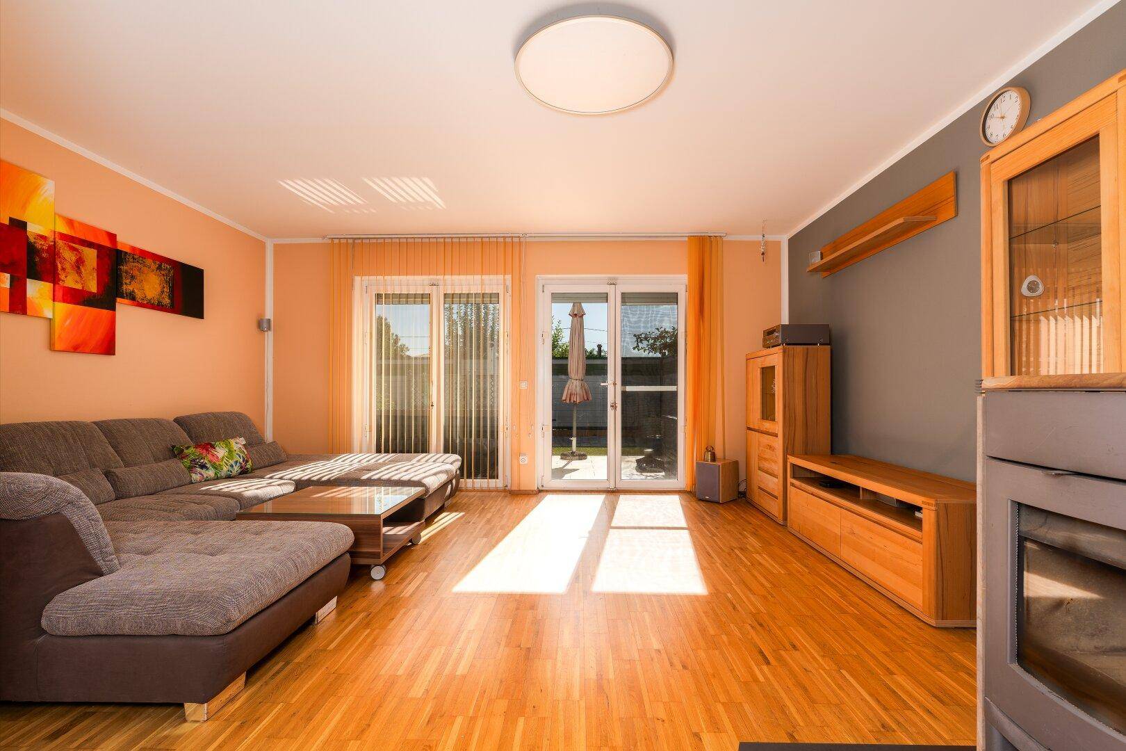 Helles Wohnzimmer mit großem Ecksofa, Holzmöbeln und einem gemütlichen Holzofen.