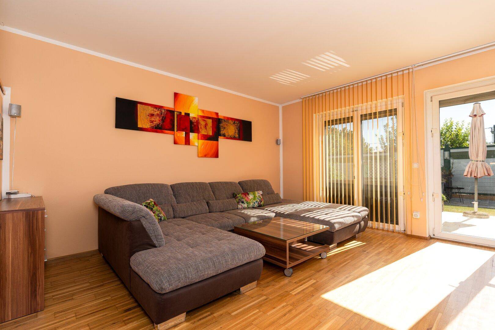 Gemütliches Wohnzimmer mit beigem Ecksofa und Zugang zur Terrasse durch große Schiebetüren.