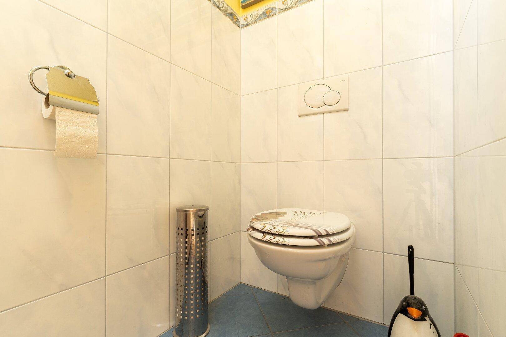 Kleines WC mit weißen Fliesen, wandhängender Toilette und blauer Bodenfliese.
