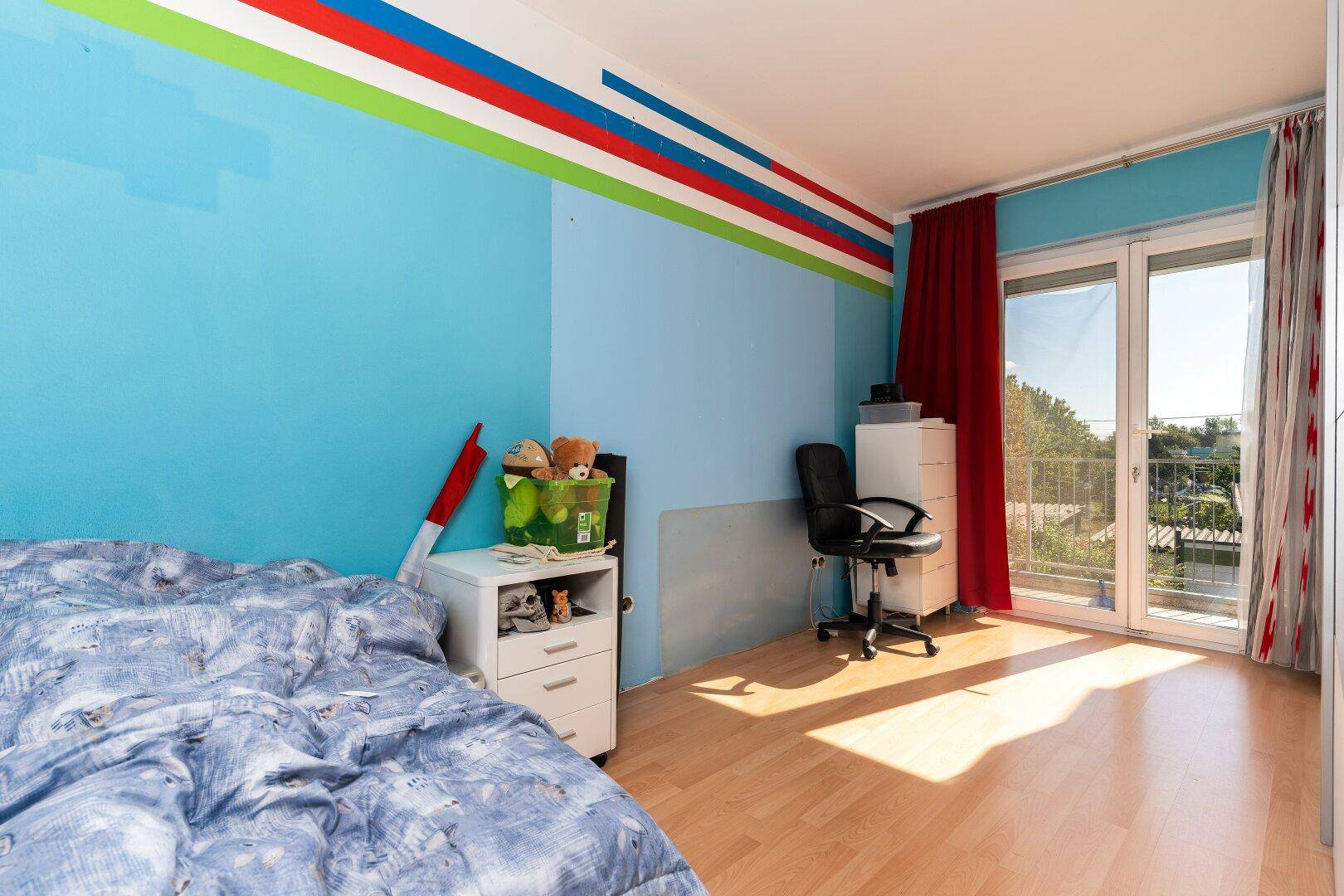 Kinderzimmer mit blauen Wänden, Holzboden und direktem Zugang zu einem Balkon.