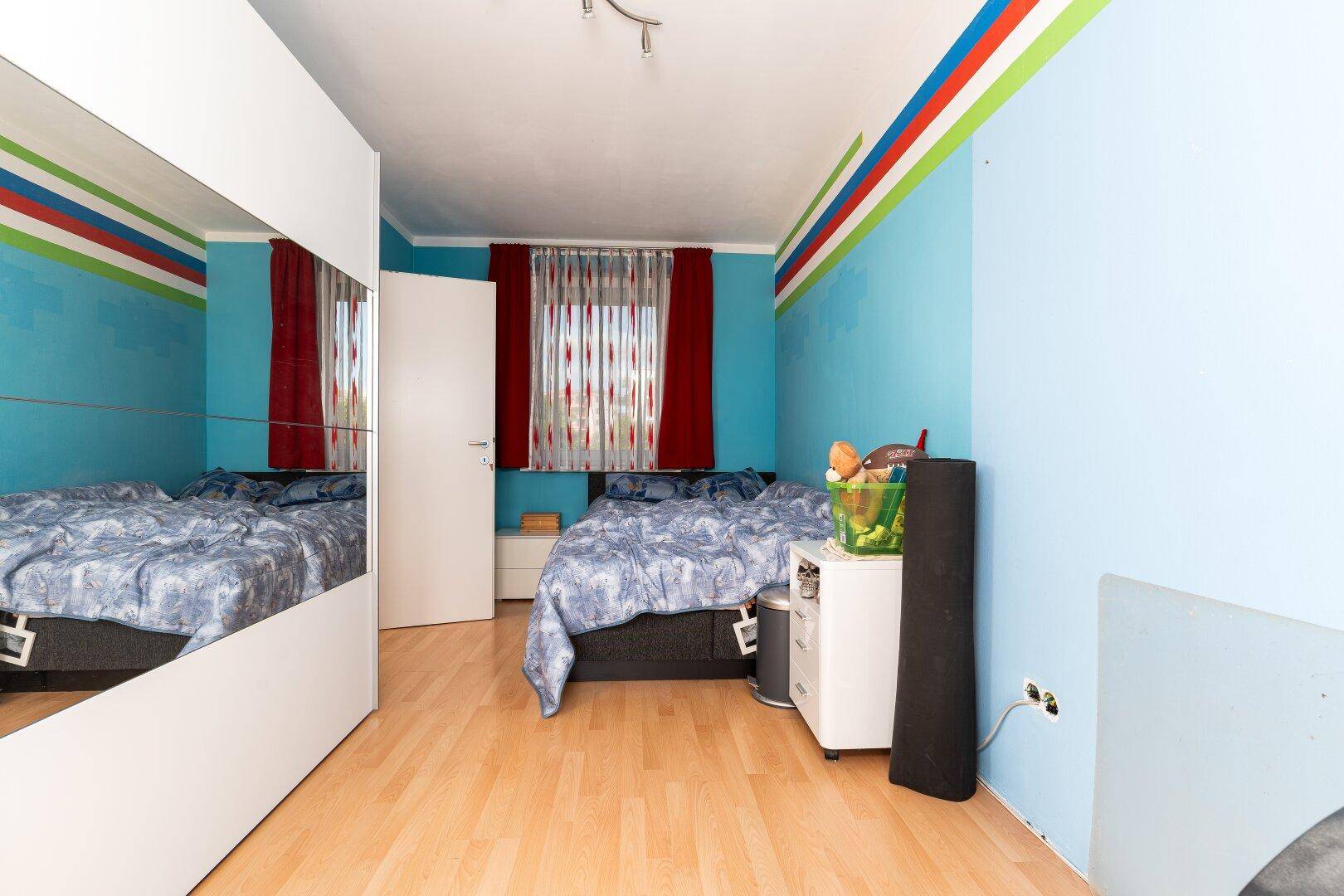 Schlafzimmer mit blauen Wänden, Holzboden und großem Spiegelschrank.