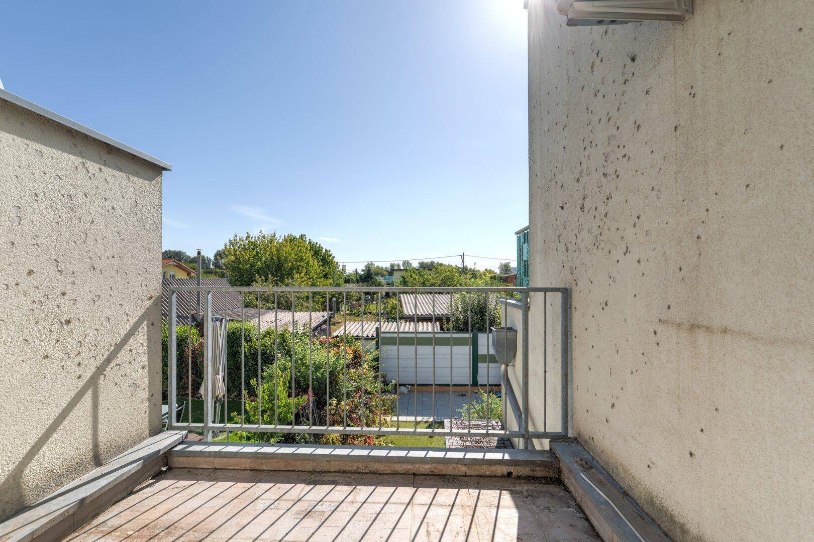 Kleiner Balkon mit Holzbelag und Metallgeländer, bietet einen Blick über die Nachbarschaft.