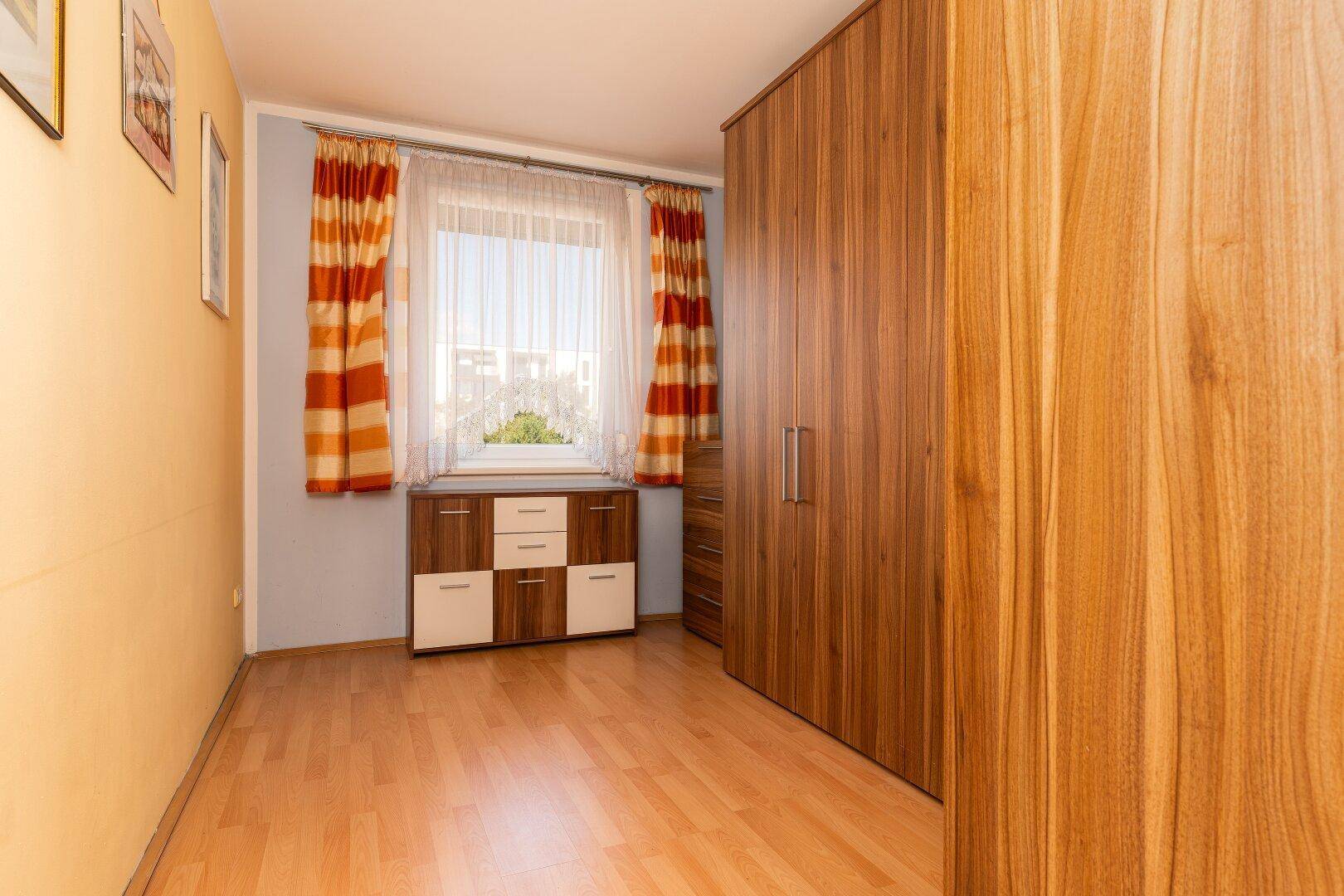 Schlafzimmer mit Holzboden, großem Holzschrank und Fenster mit Blick ins Grüne.