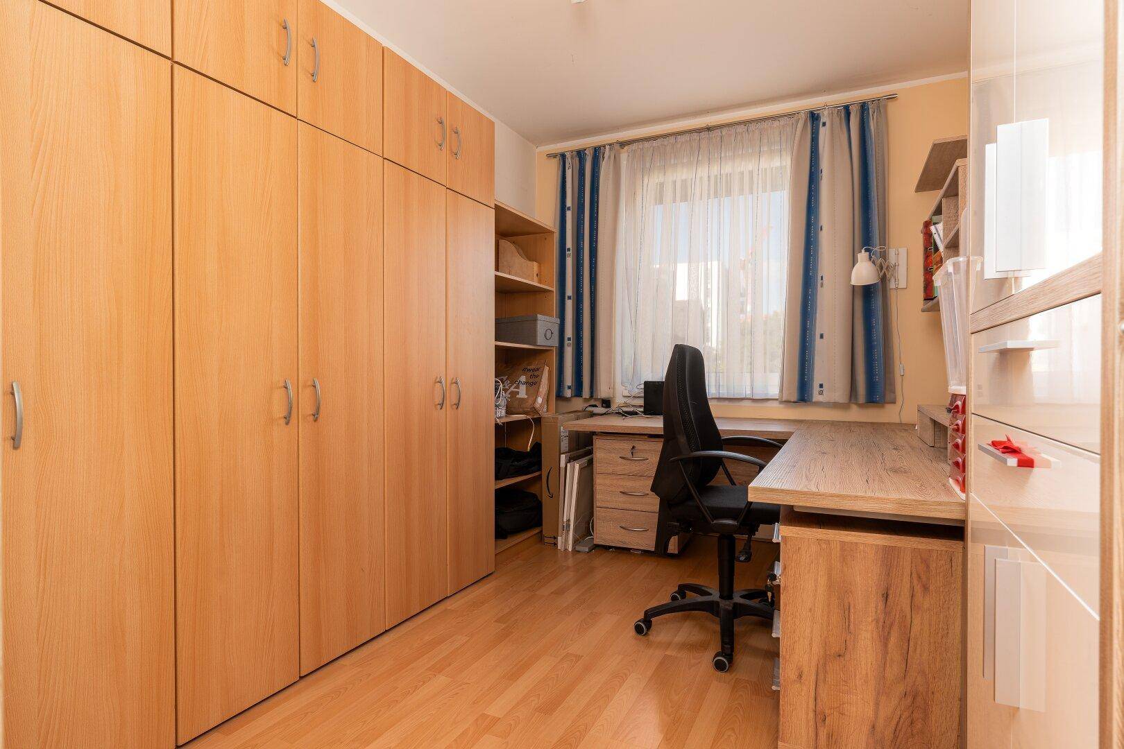 Arbeitszimmer mit vielen Holzschränken, Schreibtisch und Fenster für natürliches Licht.