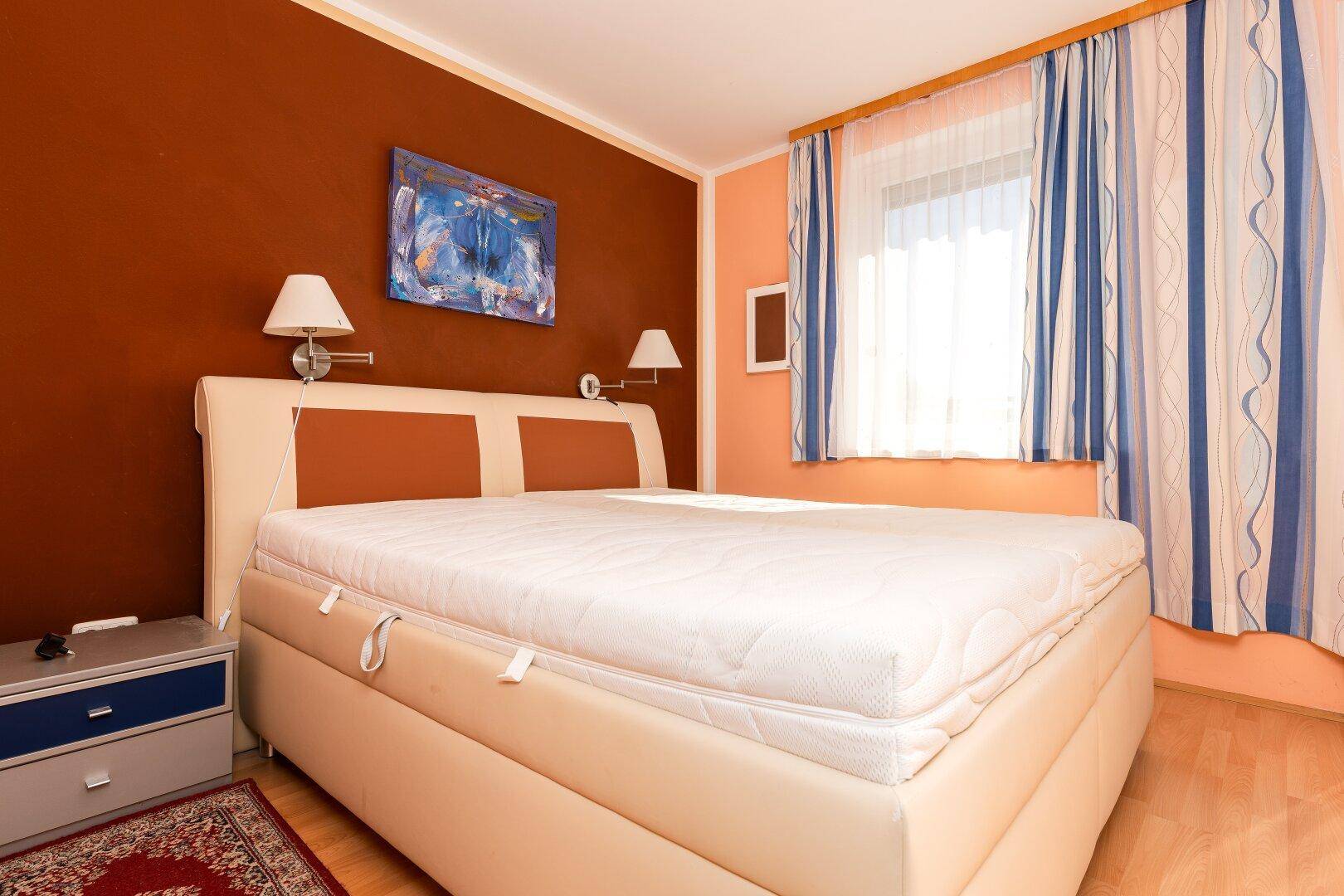 Gemütliches Schlafzimmer mit großem Bett, warmen Wandfarben und Fenster.