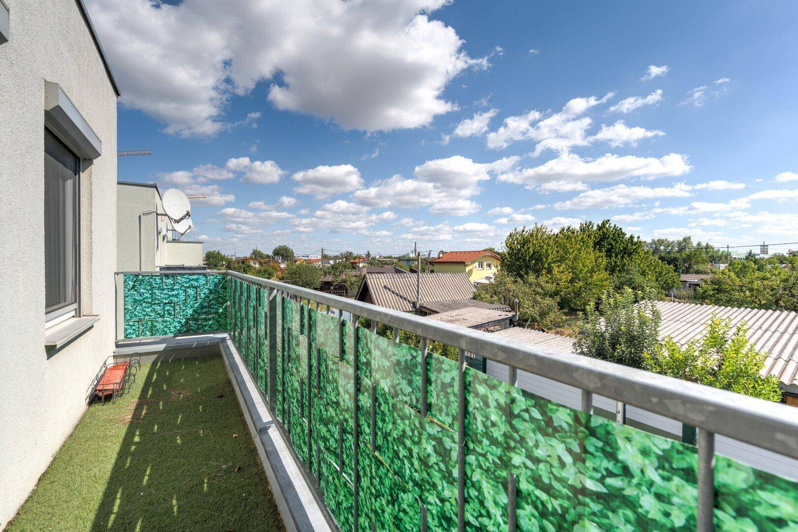 Balkon mit Kunstrasen und grüner Sichtschutzwand, bietet einen weiten Blick über die Umgebung.