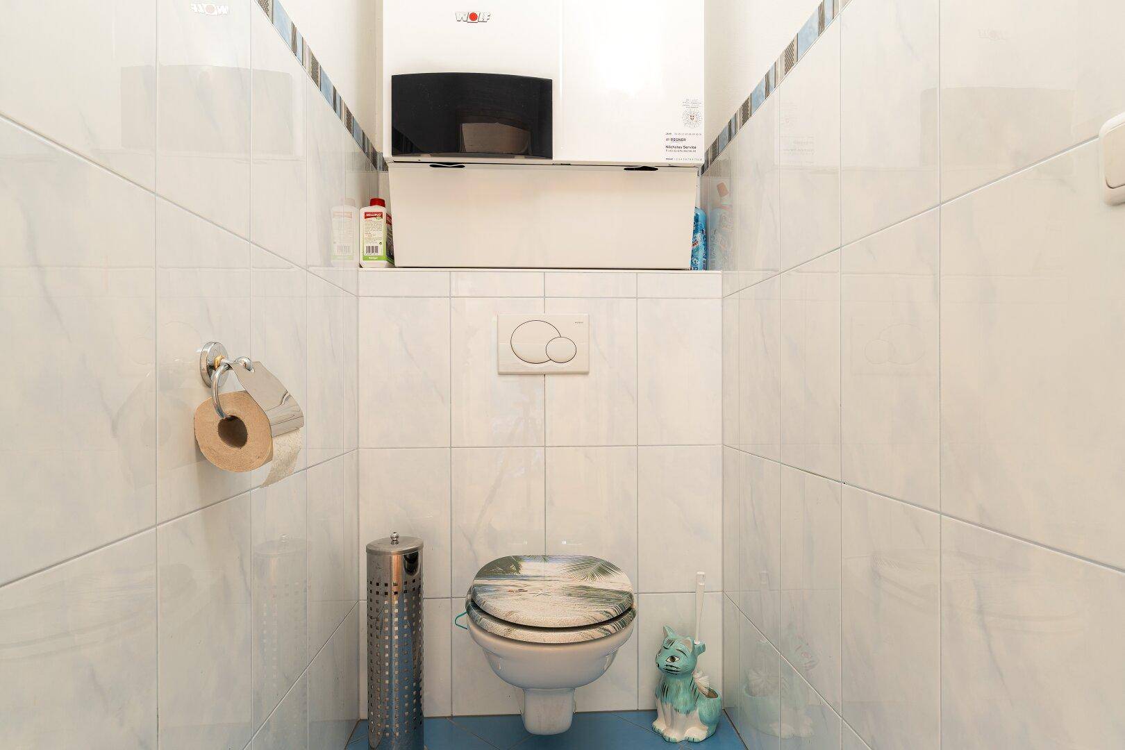 Modernes WC mit weißen Fliesen, wandhängender Toilette und integriertem Warmwasserbereiter.