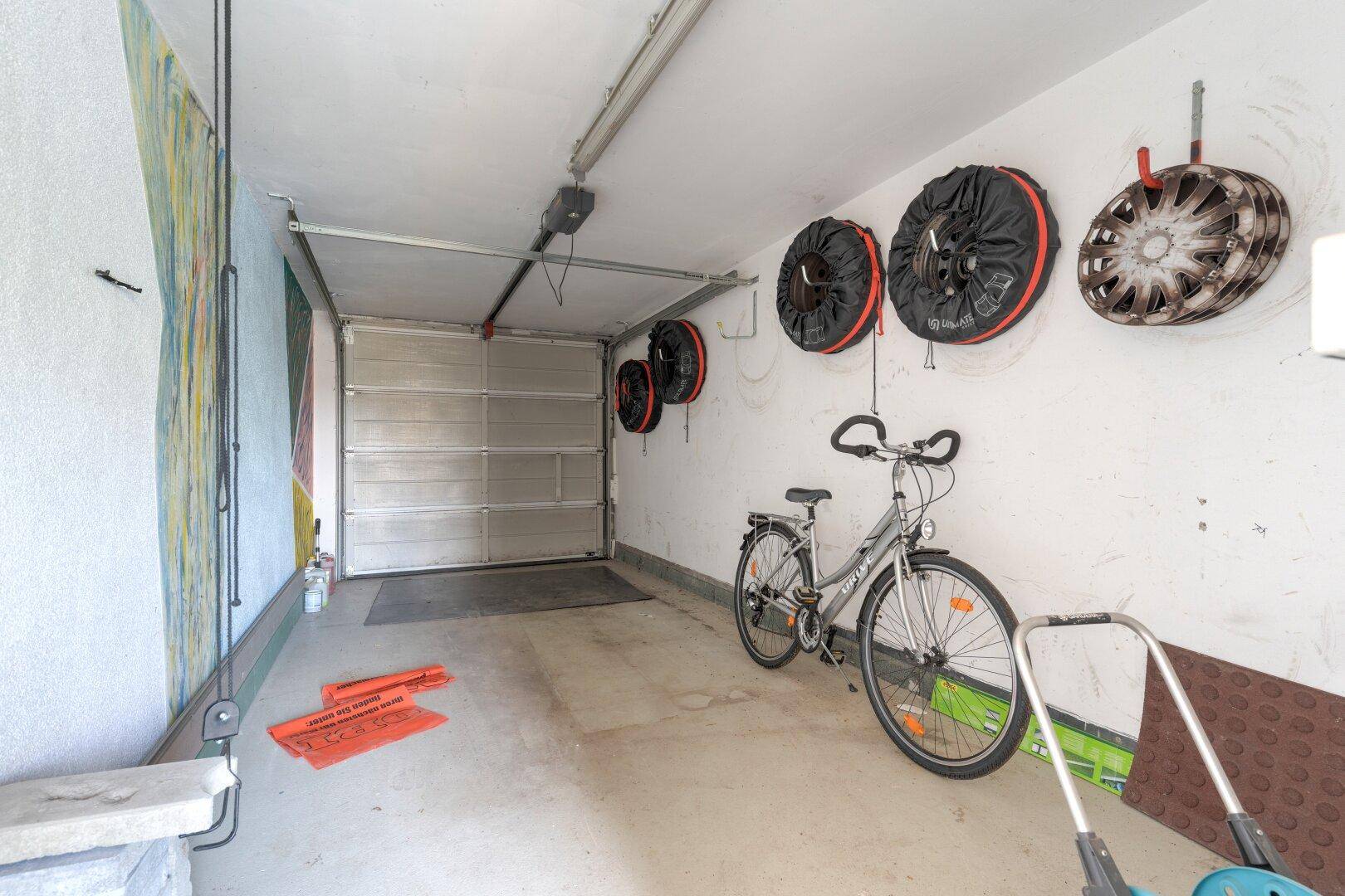 Geräumige Garage mit Betonboden, einem Fahrrad und praktischen Wandhalterungen für Reifen.