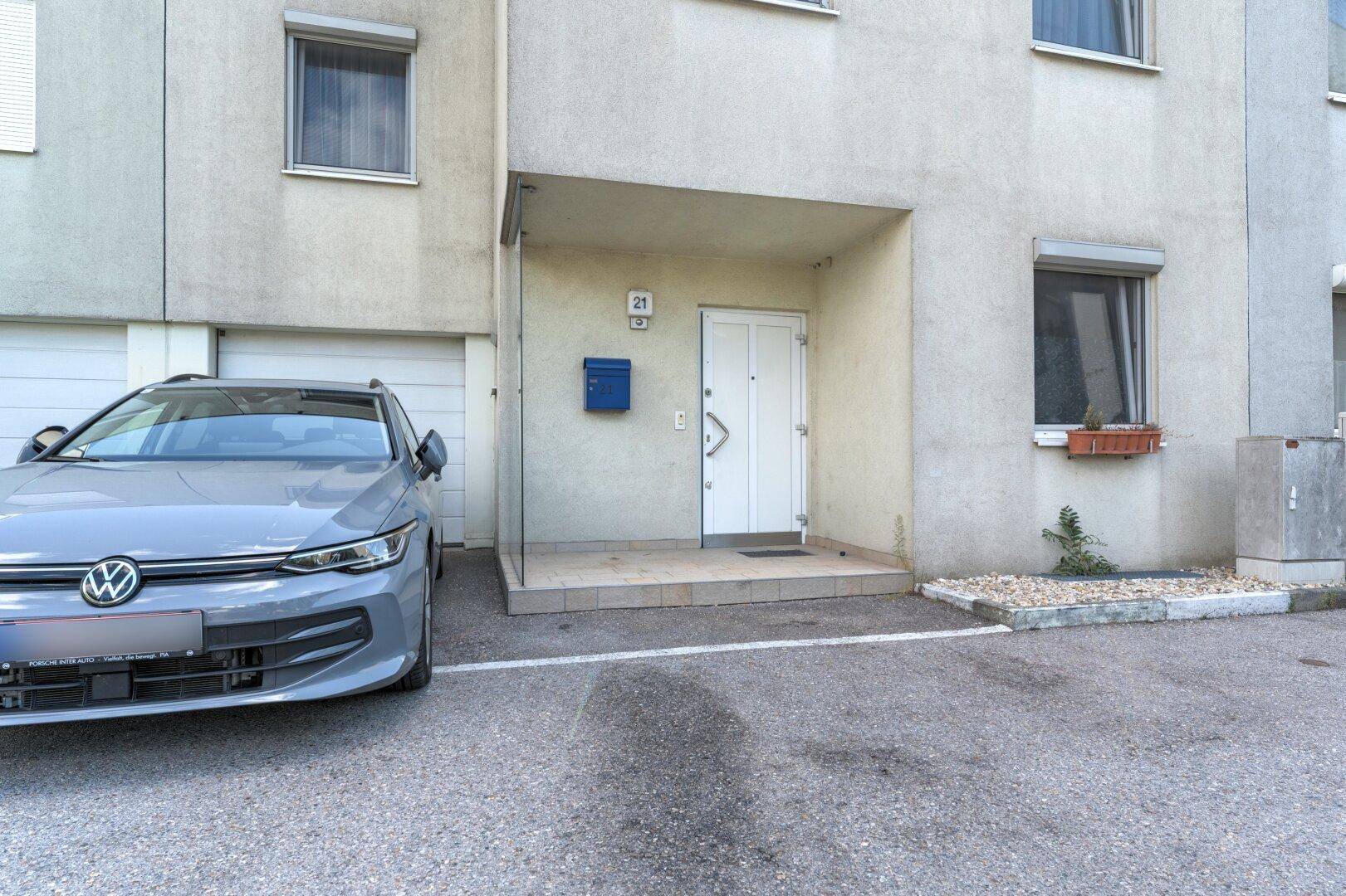 Eingangsbereich eines modernen Reihenhauses mit geparktem Auto und Garagenzufahrt.