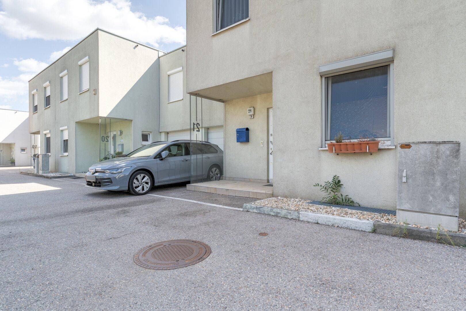 Außenansicht eines Reihenhauses mit moderner Architektur, Parkplatz und Rollläden an den Fenstern.