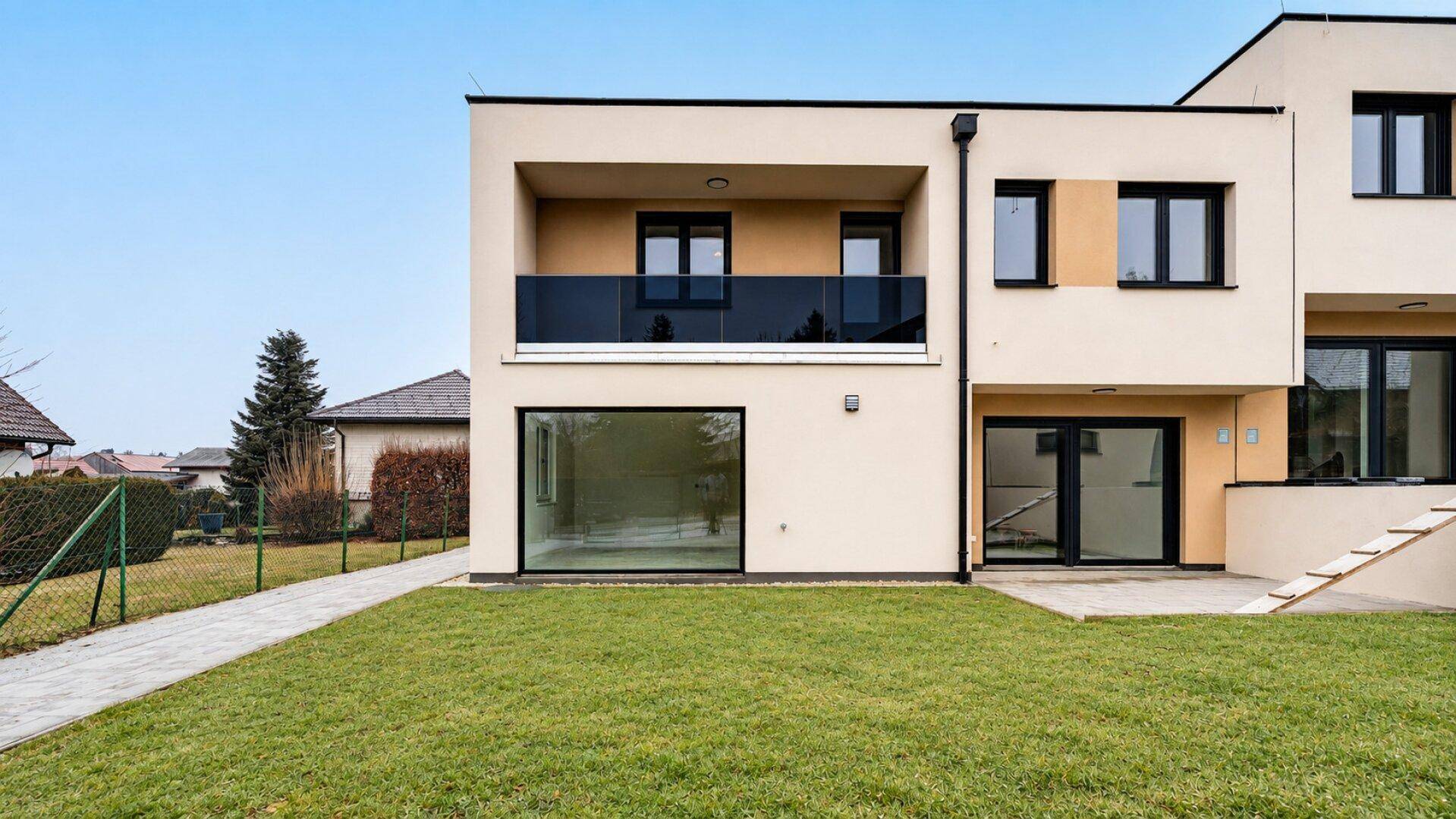 Nahaufnahme der modernen Reihenhausfassade mit Balkon und Zugang zum grünen Garten.