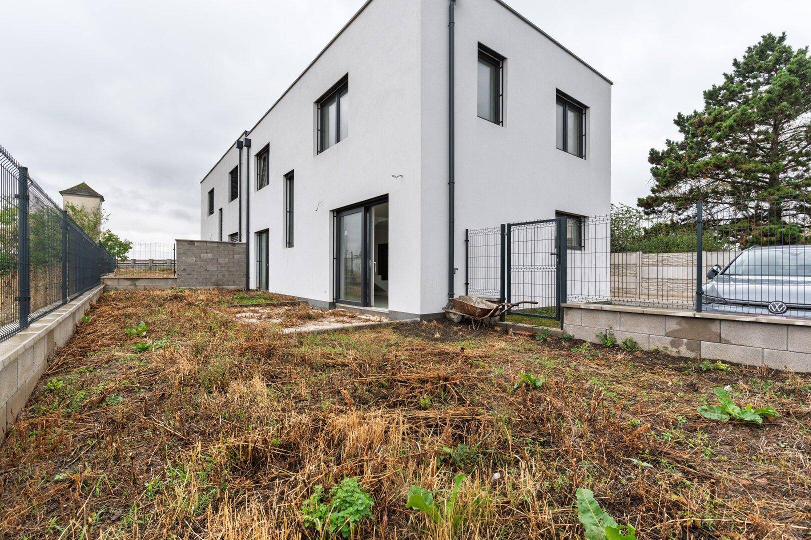 Außenansicht des Neubaus mit unfertigem Gartenbereich und Zaun.