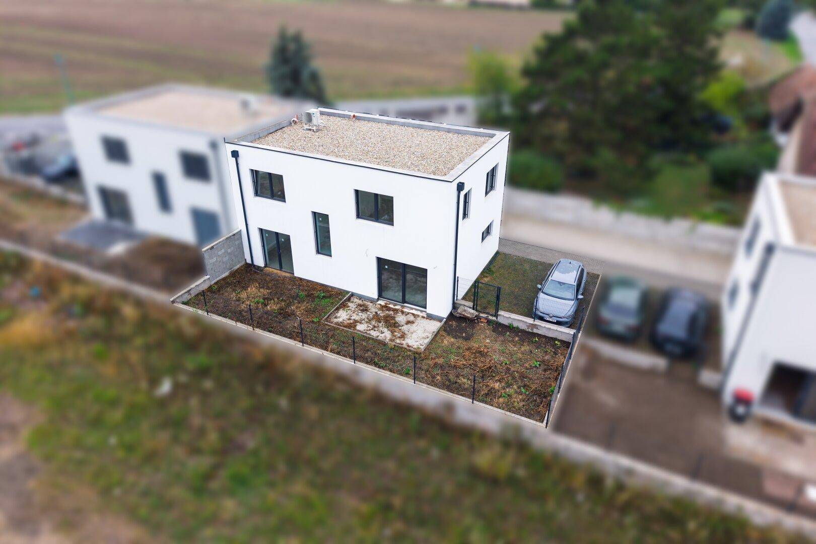 Luftaufnahme eines modernen Neubaus mit Garten und Parkplatz.