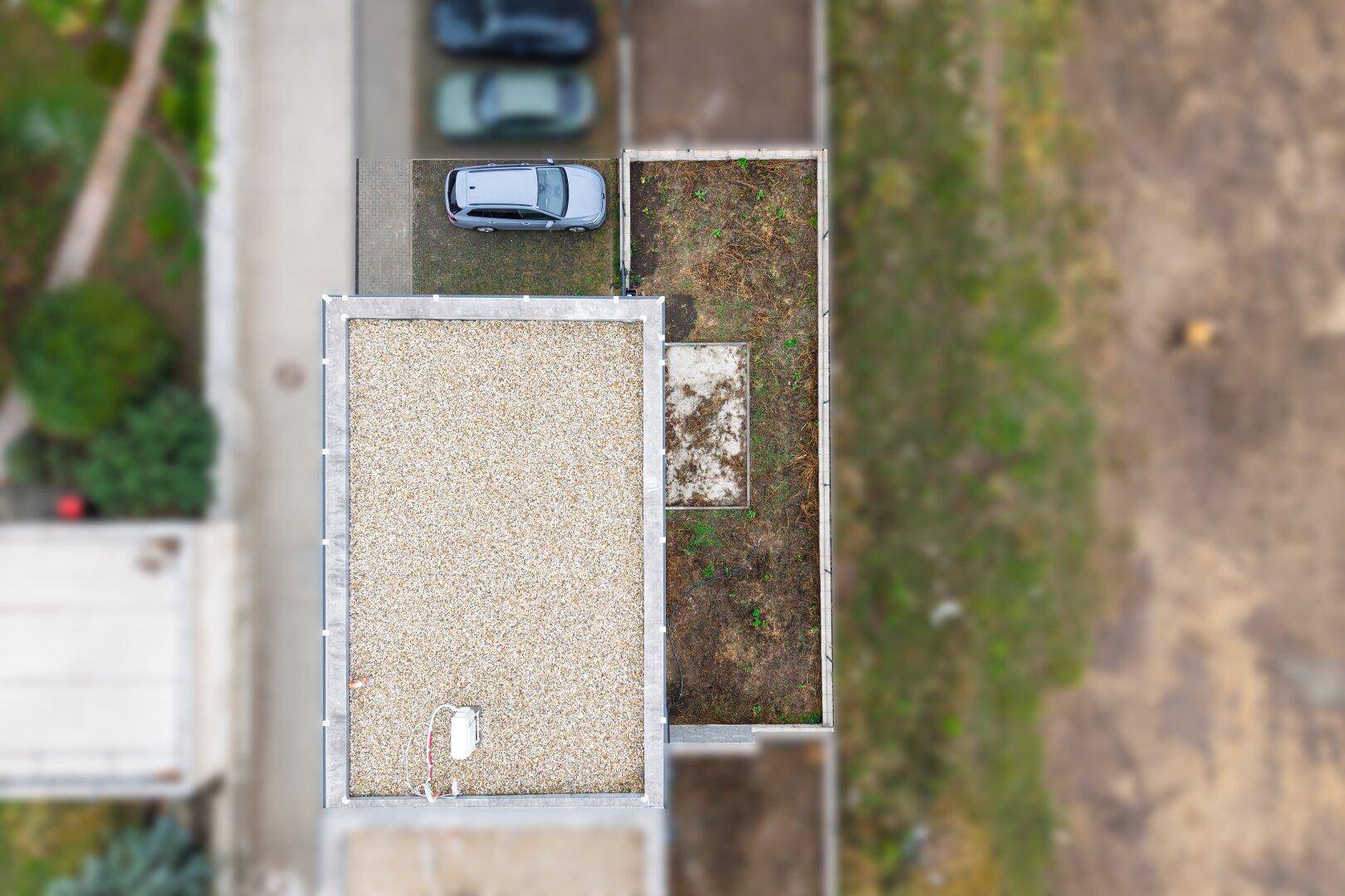 Vogelperspektive eines Flachdachhauses mit Parkplatz und begrüntem Dachbereich.