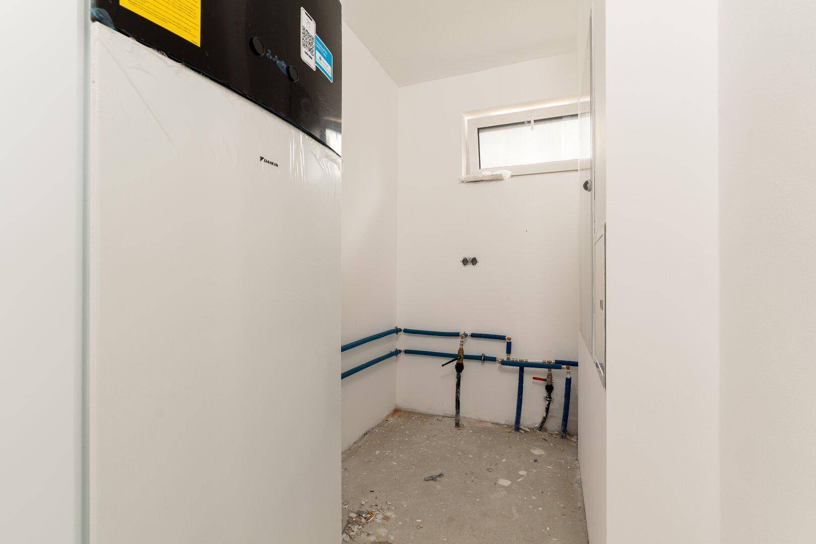 Technikraum mit Warmwasserbereiter und sichtbaren Wasserleitungen im Rohbau.