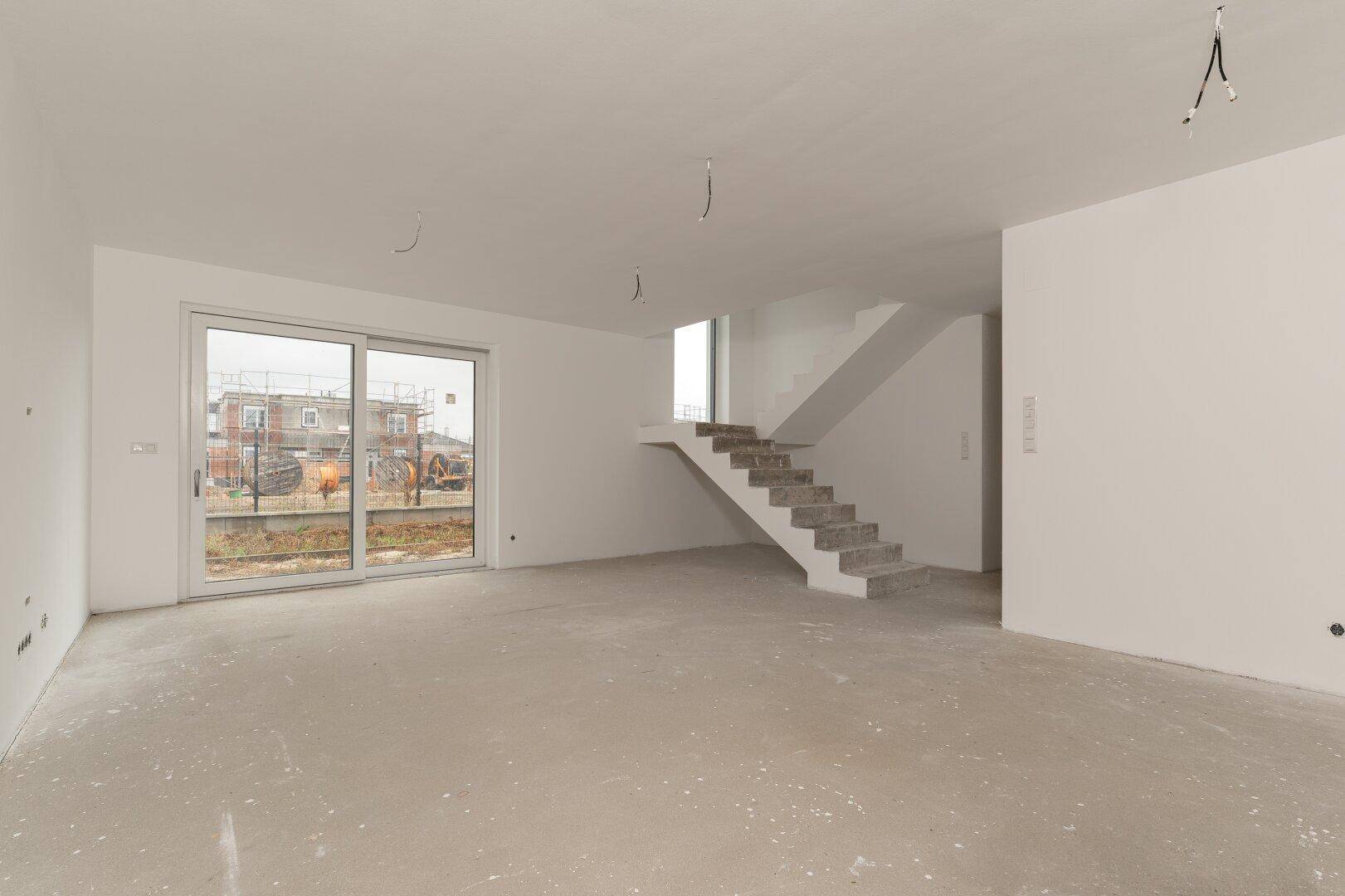 Geräumiger, unfertiger Wohnbereich mit Treppe und Zugang zum Außenbereich.