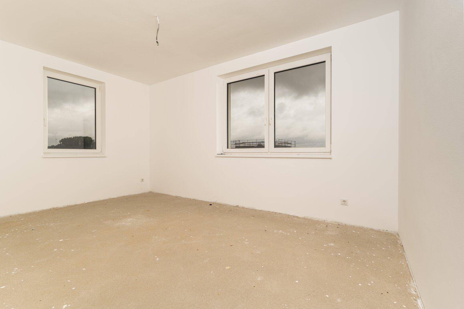 Helles Zimmer im Rohbau mit zwei Fenstern und Blick auf die Umgebung.