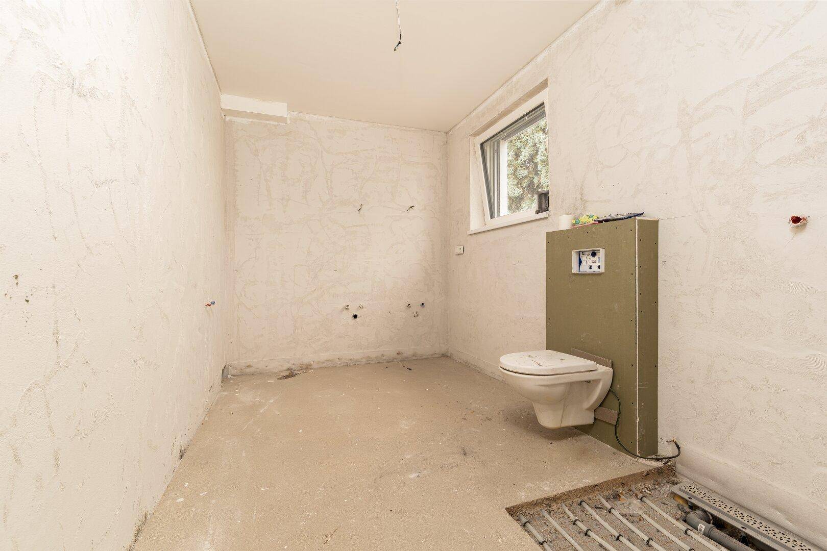 Unfertiges Badezimmer mit vorbereiteter Toilette und Fußbodenheizung.