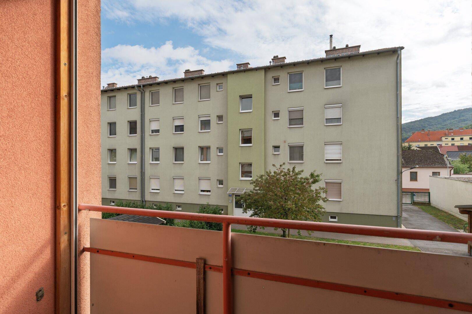 Balkon mit Blick auf ein mehrstöckiges Wohngebäude und bewölkten Himmel.