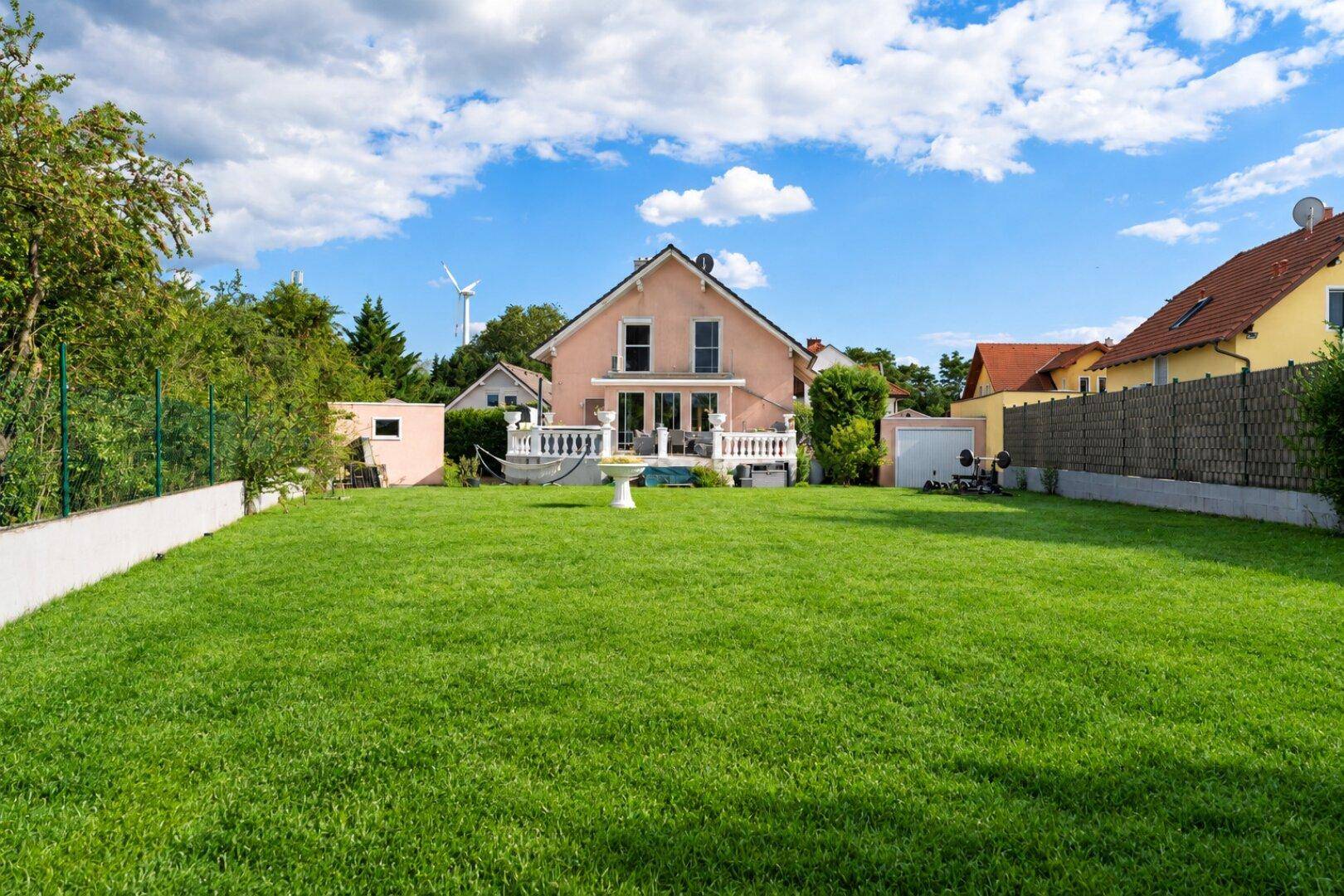 Gepflegter großer Garten mit Rasenfläche und Blick auf das rosa Einfamilienhaus.