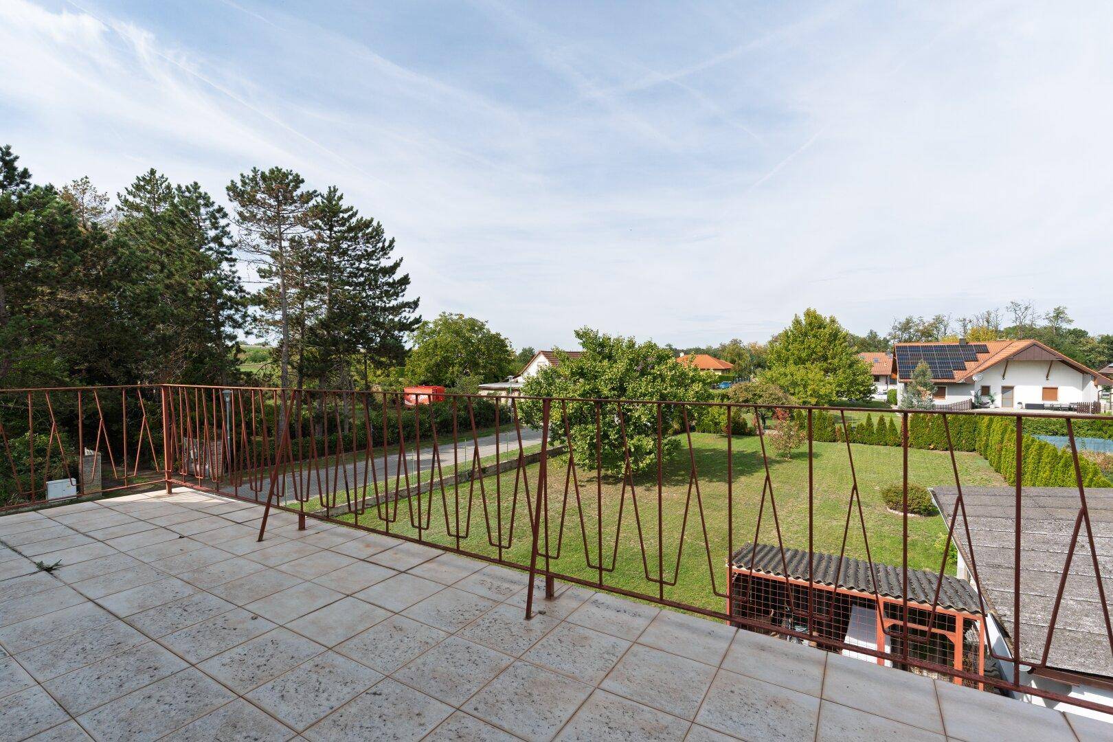 Großer Balkon mit Metallgeländer und weitem Blick über den Garten und die ländliche Umgebung.