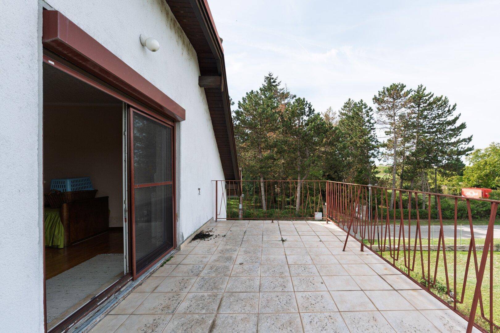 Großer gefliester Balkon mit Metallgeländer und weitem Blick in die Natur.