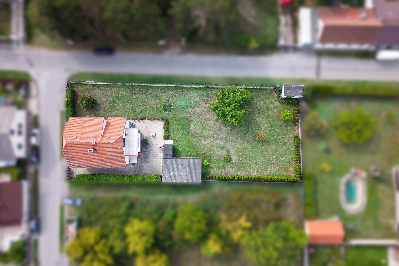 Vogelperspektive des Grundstücks mit Haus, Garage, Terrasse und weitläufigem Rasenbereich.