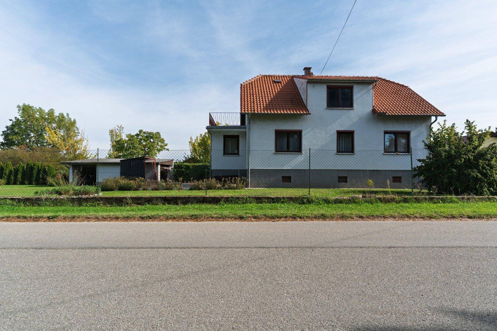 Rückansicht des Einfamilienhauses mit Garten, Zaun und einem Nebengebäude im Hintergrund.