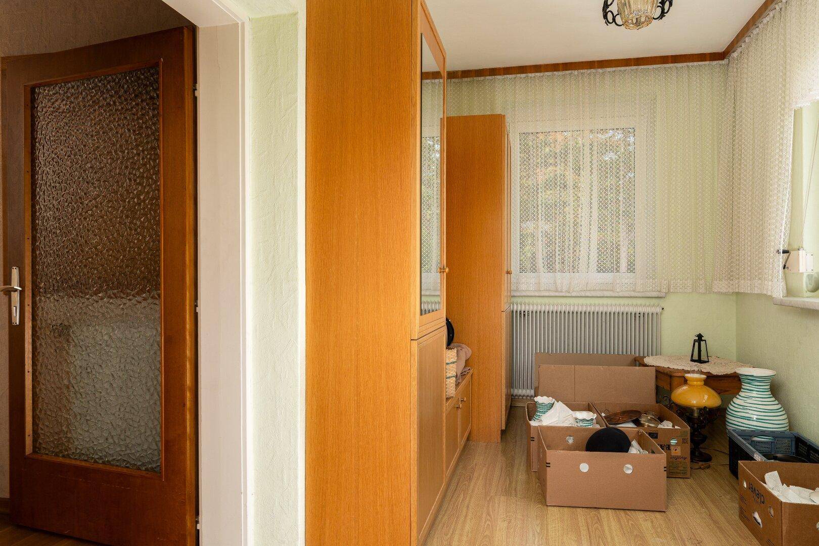 Innenraum mit Laminatboden, Fenster und verschiedenen Kartons, die auf einen Umzug hindeuten.
