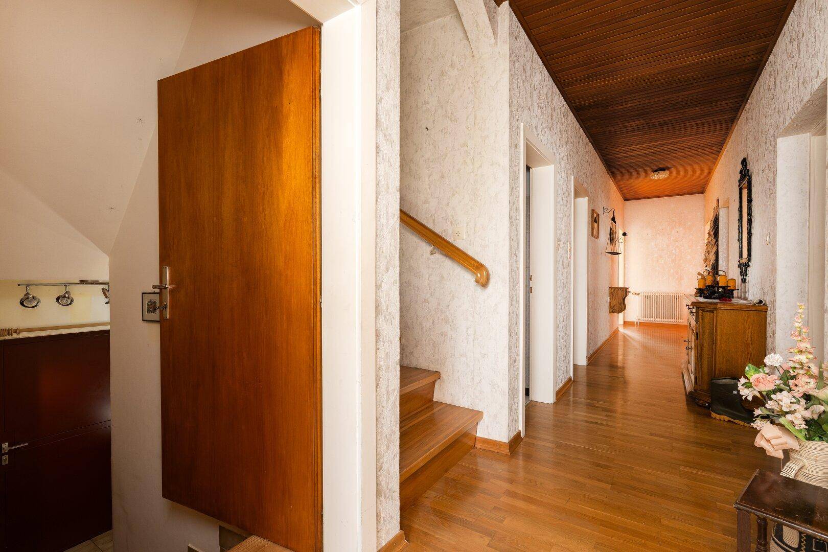 Heller Flur mit Holztreppe, Holzdecke und traditioneller Tapete.