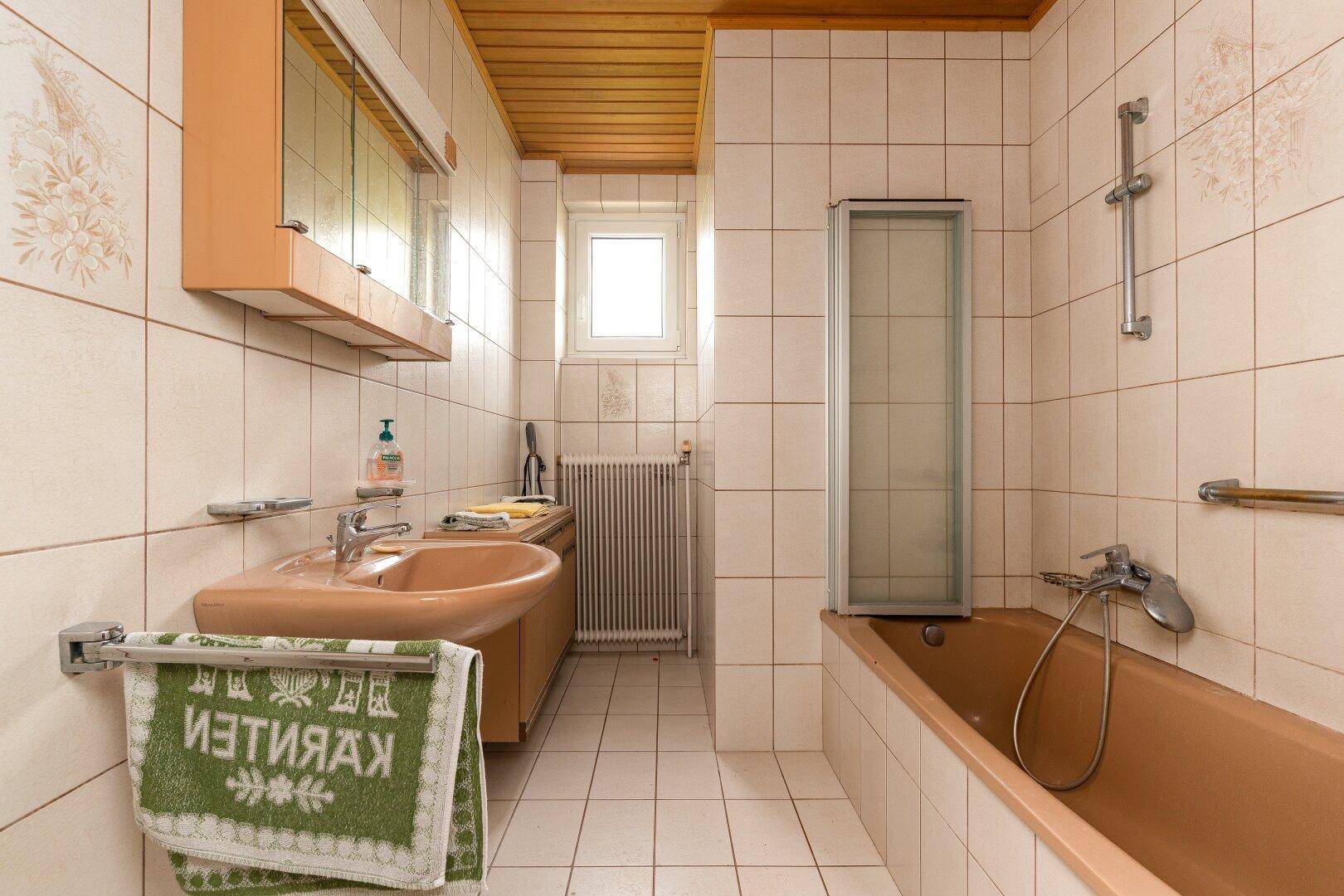Badezimmer im Stil der 80er Jahre mit brauner Badewanne, Doppelwaschbecken und Fenster.