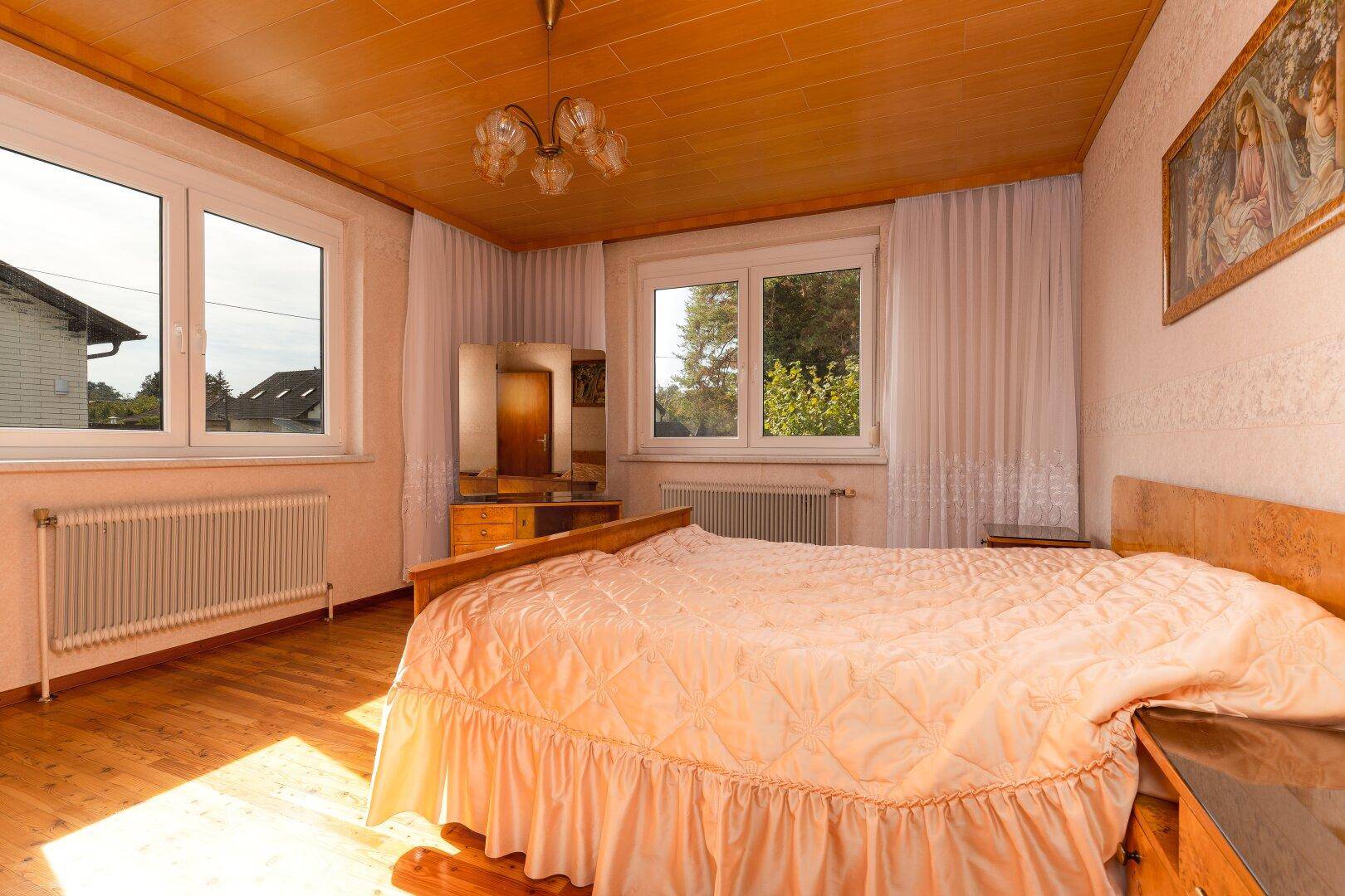 Schlafzimmer mit Holzdecke, Doppelbett und zwei Fenstern, die viel Licht hereinlassen.
