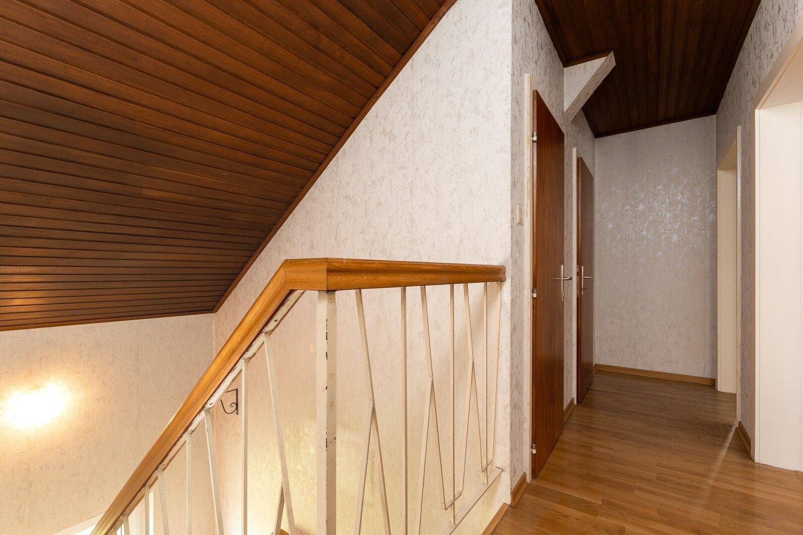 Treppenhaus mit Holzgeländer und Holzdecke, das die oberen Stockwerke verbindet.