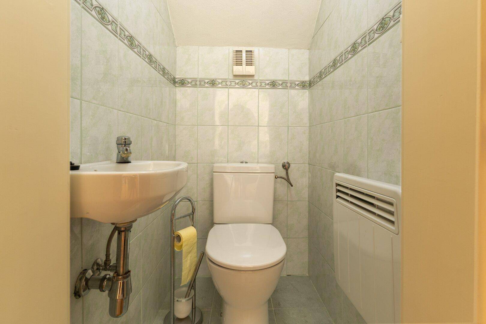 Kleines Gäste-WC mit hellgrünen Fliesen, Waschbecken und Toilette.