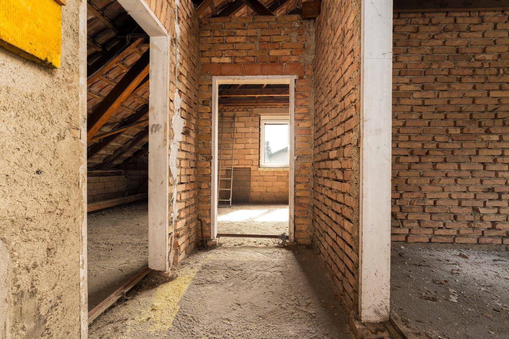 Dachboden im Rohbau mit sichtbaren Ziegelwänden und Holzbalken, bereit für Ausbau.