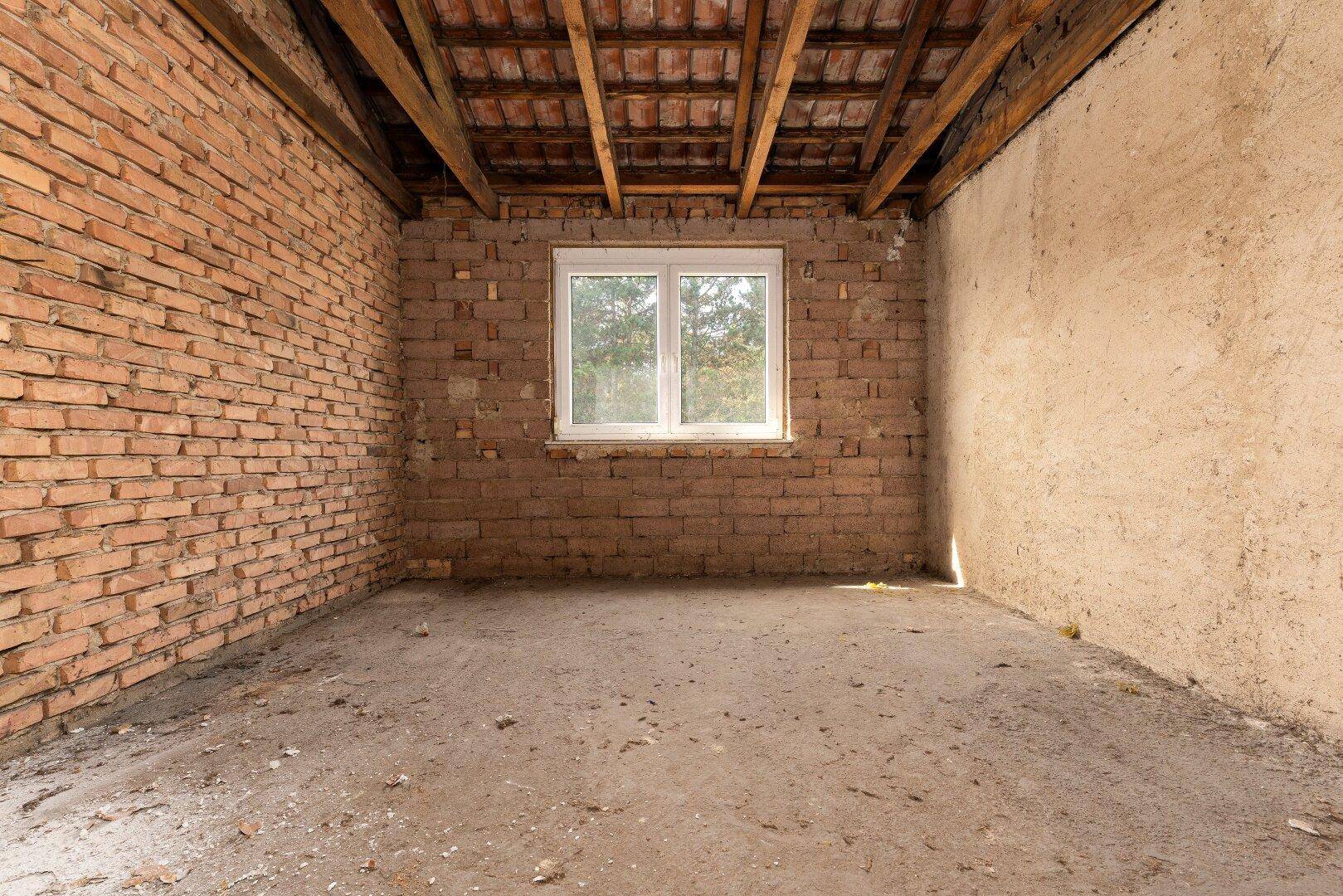 Dachbodenraum mit Ziegelwänden und Fenster, ideal für zukünftigen Ausbau.