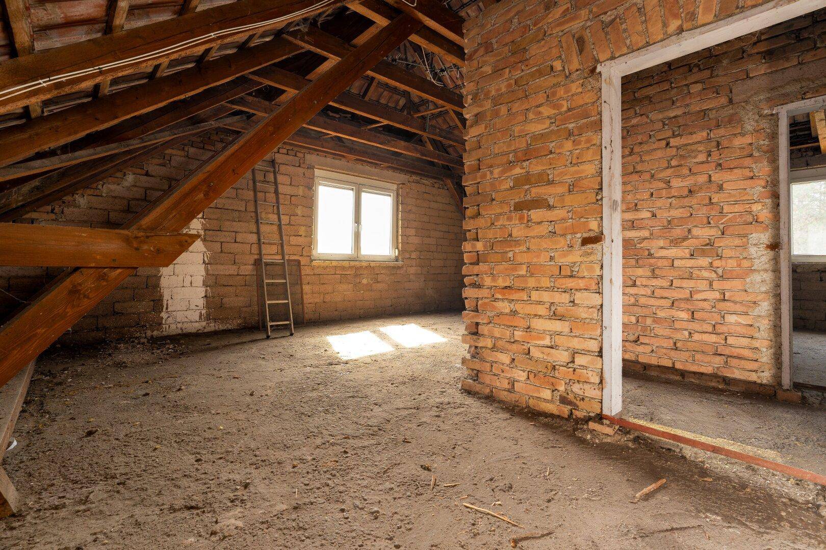Geräumiger Dachbodenbereich mit sichtbaren Holzbalken und Ziegelwänden, bereit zum Ausbau.
