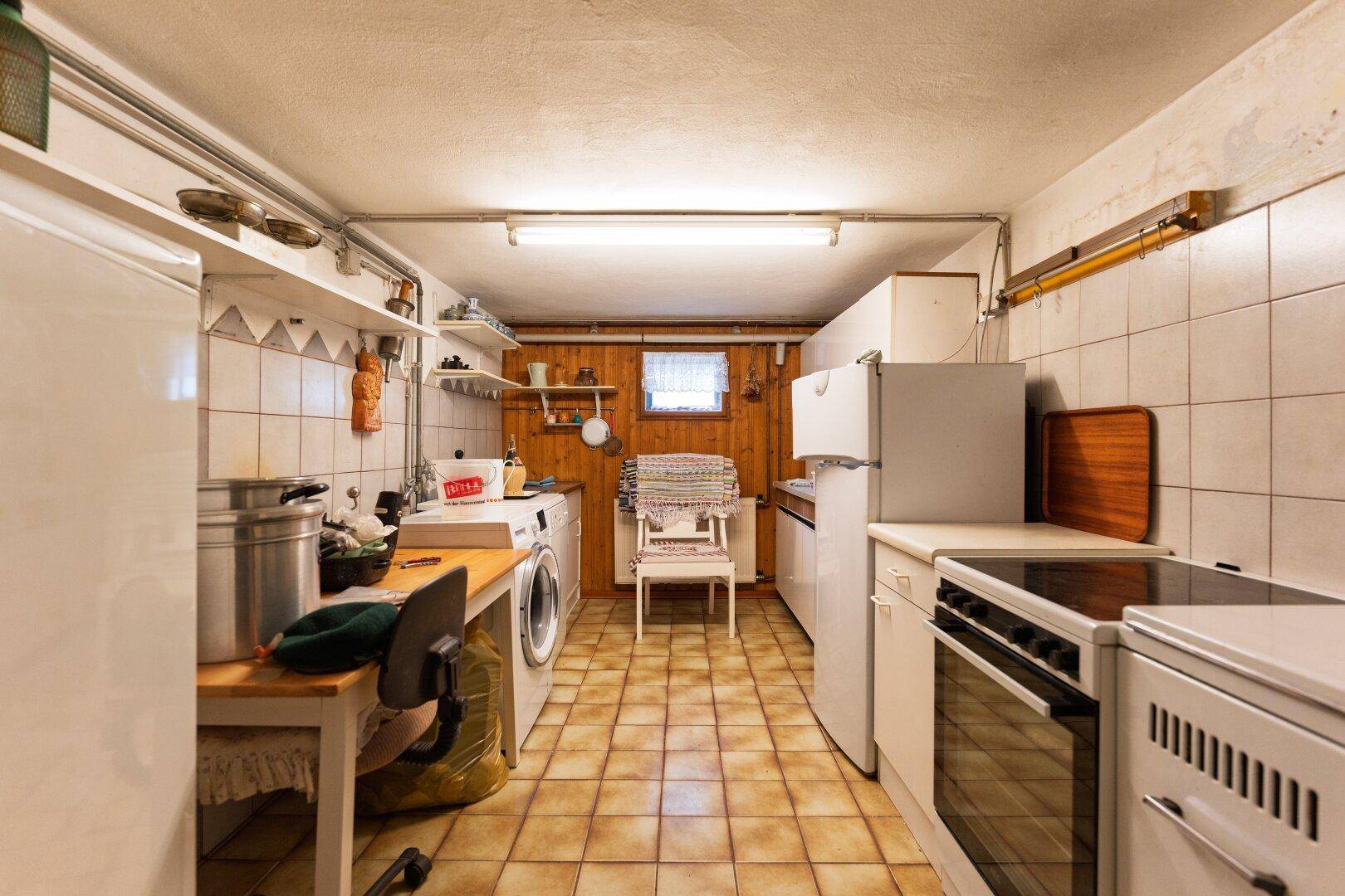 Funktionale Waschküche im Keller mit Waschmaschine, Spüle und einfachen Fliesen an Wänden und Boden.
