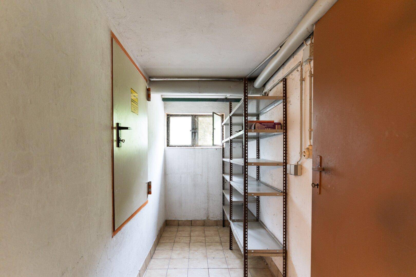 Schmaler Abstellraum im Keller mit Metallregalen und einem kleinen Fenster für Belüftung.