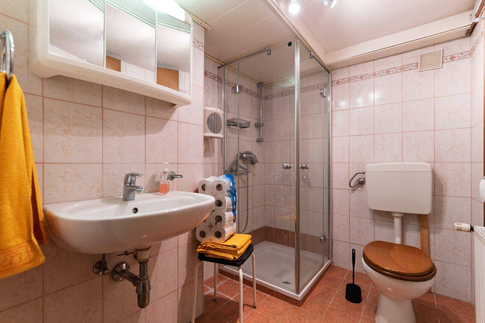 Kleines Badezimmer mit Dusche, WC, Waschbecken und orangefarbenen Fliesen im 80er-Jahre-Stil.