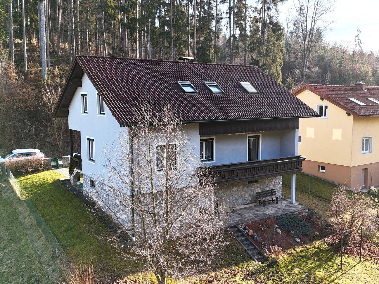 Seitenansicht des Hauses mit Balkon und Steinsockel, umgeben von Natur.