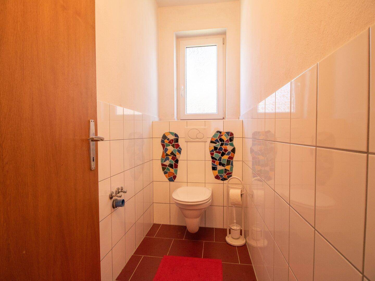 Separate Toilette mit Fenster und farbigen Fliesenakzenten, hell und funktional.