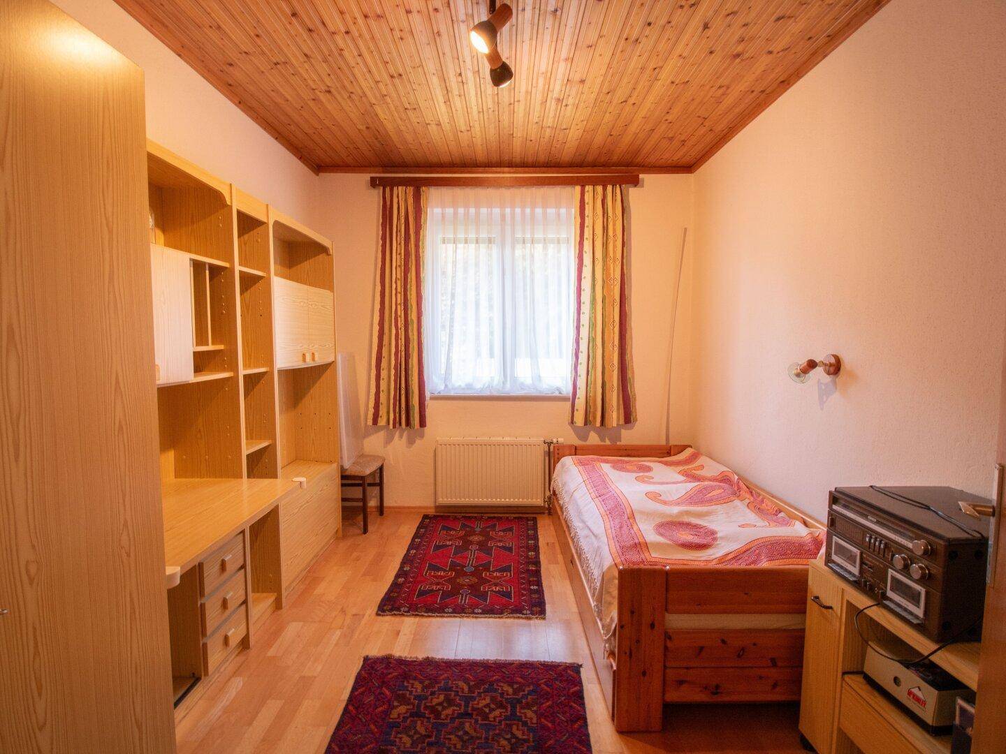 Schlafzimmer mit Holzbalkendecke, Einzelbett und integriertem Schreibtischbereich.