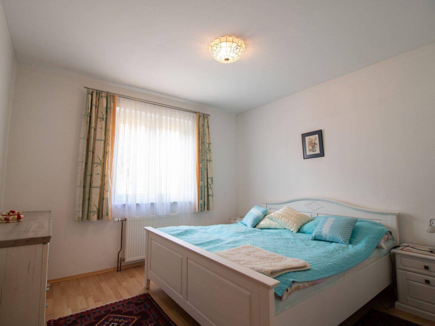 Helles Schlafzimmer mit Doppelbett und Fenster, schlicht und funktional eingerichtet.