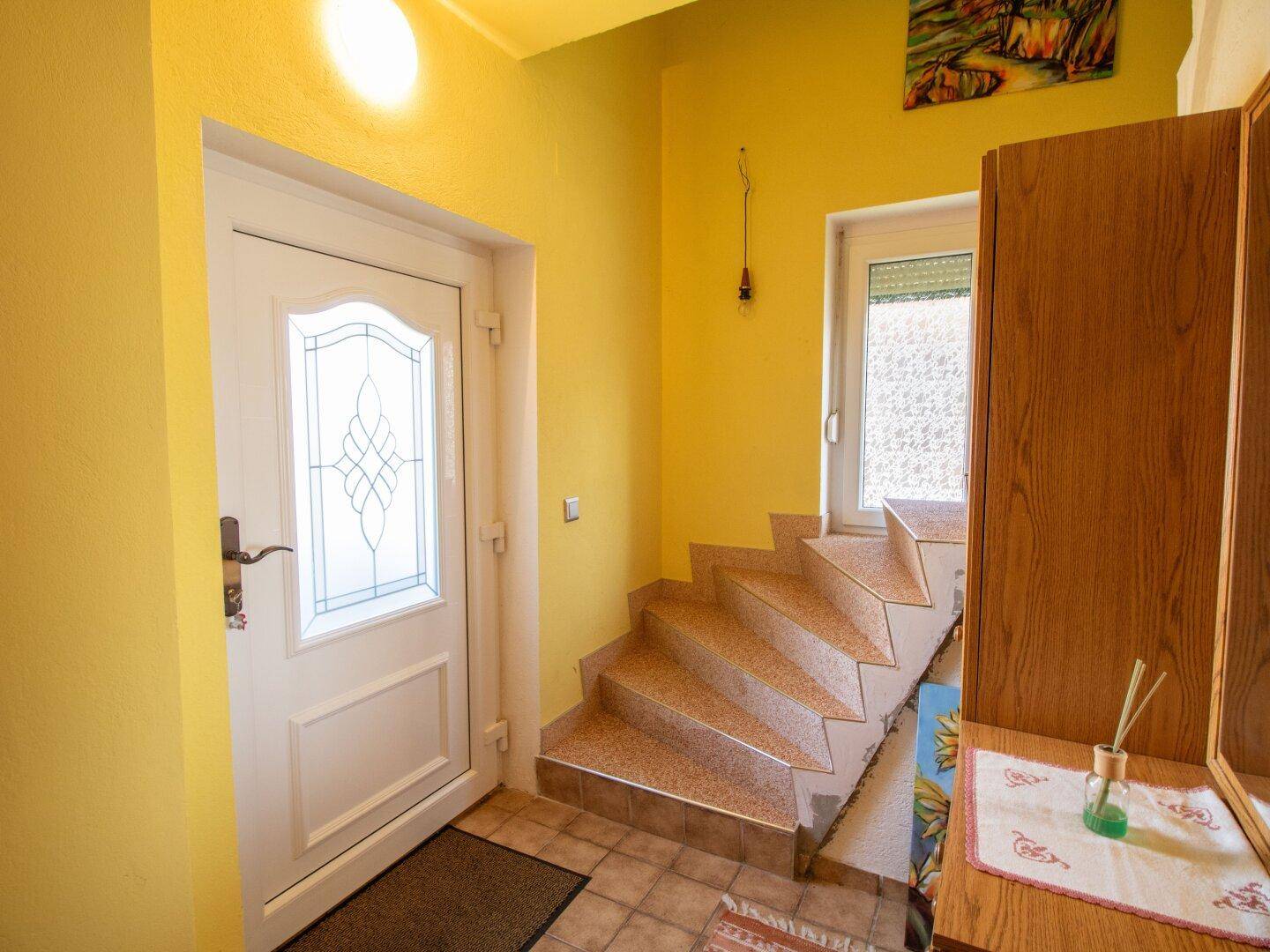 Heller Eingangsbereich mit Treppe und Garderobe, gelb gestrichene Wände.