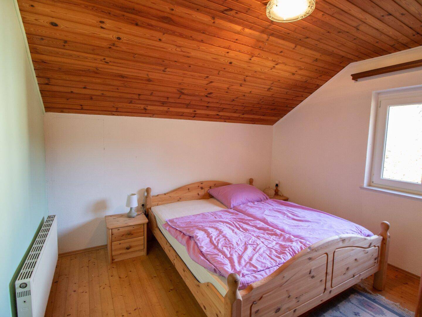 Schlafzimmer mit Holzdecke, Doppelbett und Holzboden, gemütlich eingerichtet.