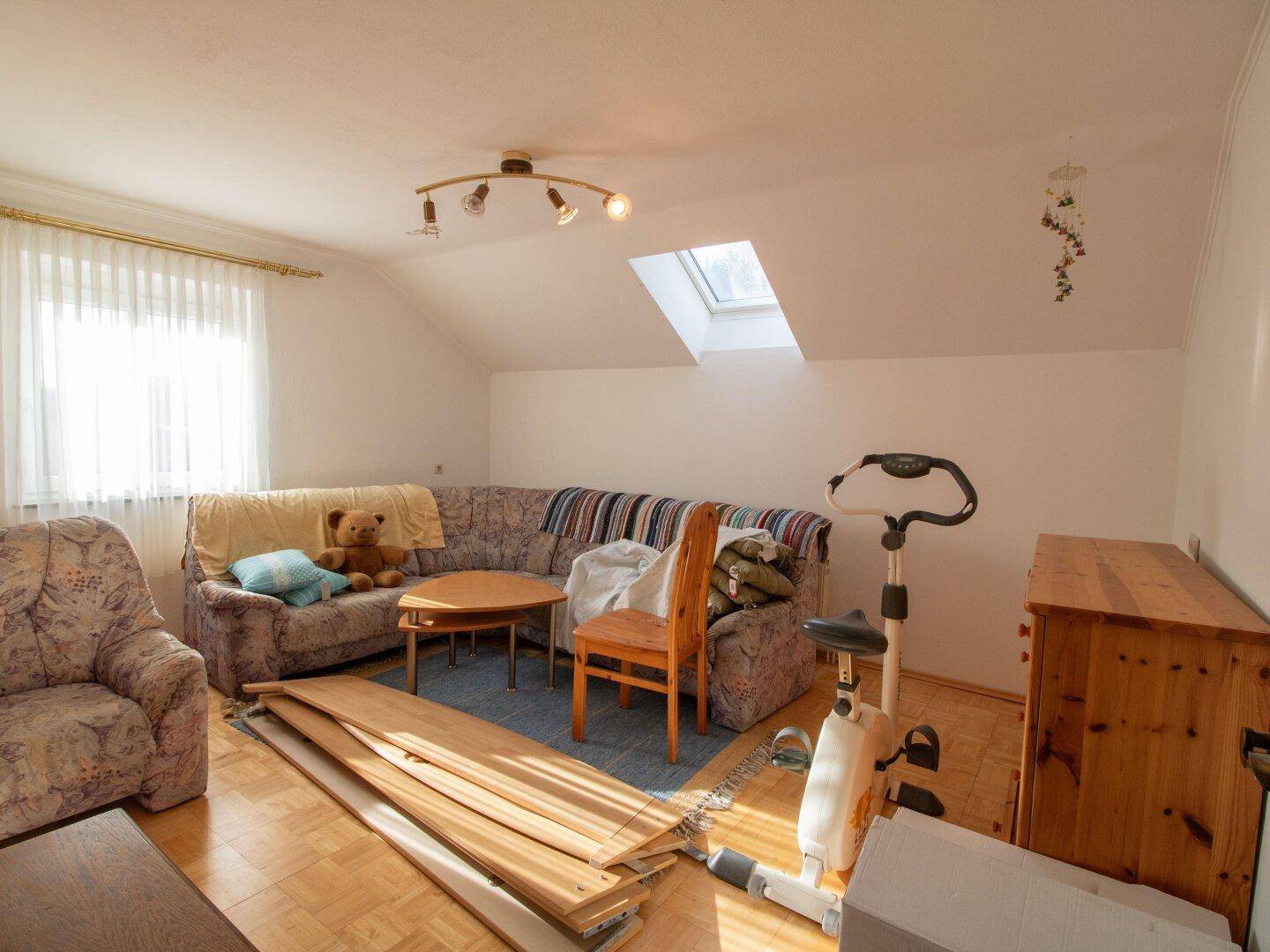 Helles Dachgeschoss-Wohnzimmer mit Sofa, Dachfenster und Parkettboden.