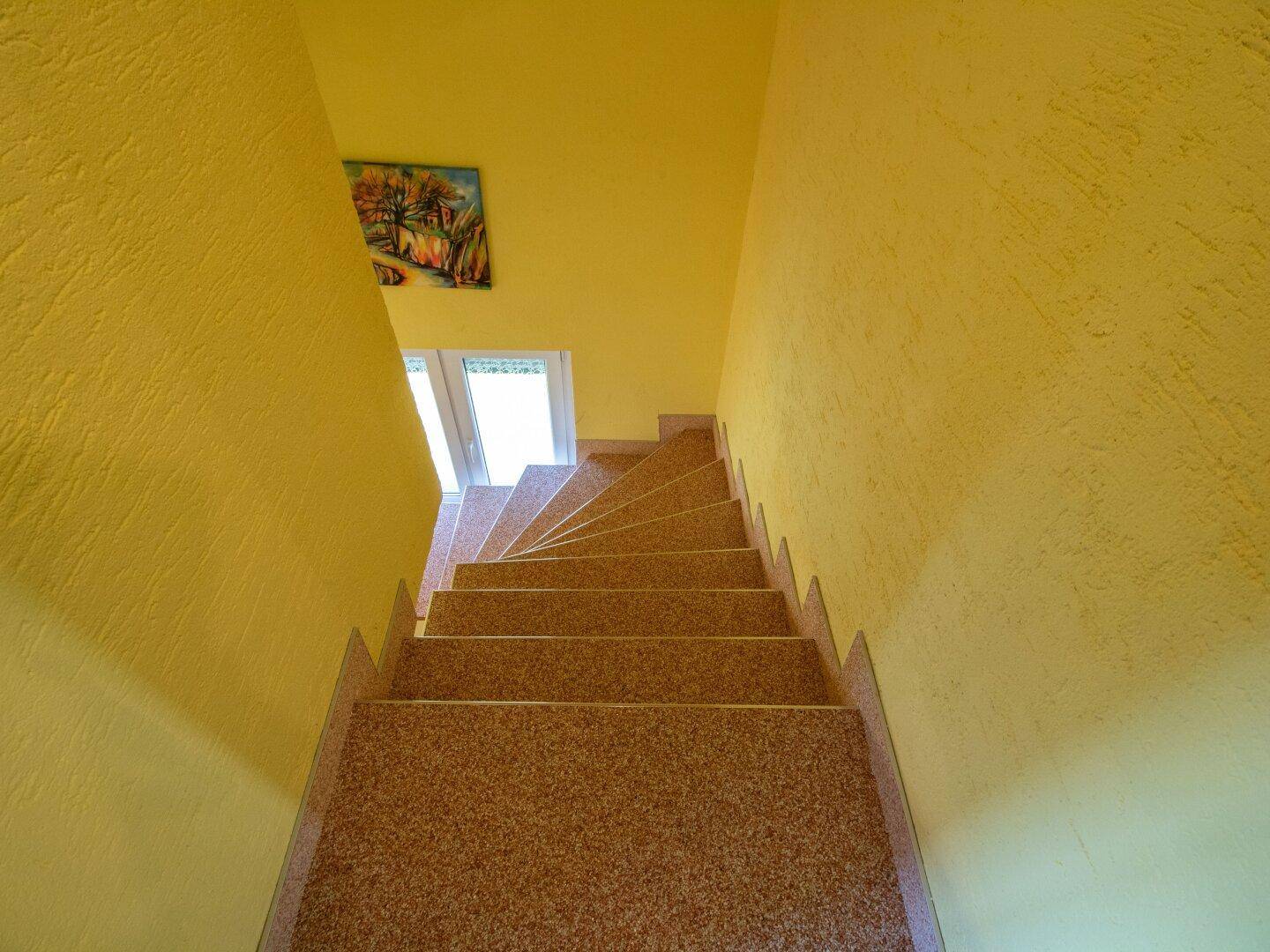 Treppenaufgang mit gelben Wänden und Blick nach unten, gut beleuchtet.