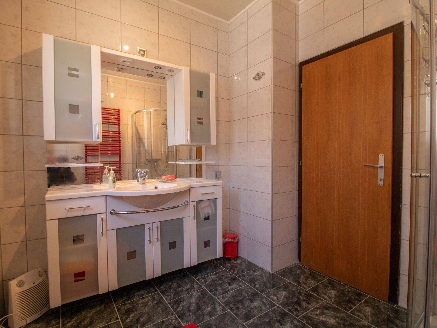Badezimmer mit Waschtischunterschrank, Spiegelschrank und Duschkabine.