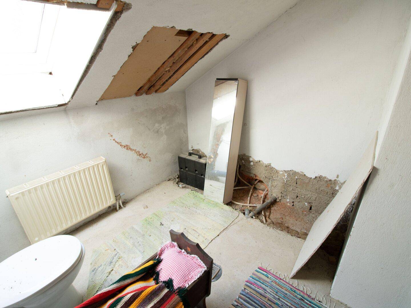 Badezimmer im Rohbauzustand mit Dachfenster und Heizkörper, renovierungsbedürftig.